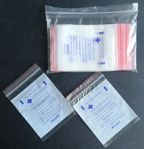 Clear resealable pill bags with blue printing, one pack and two loose bags on dark surface