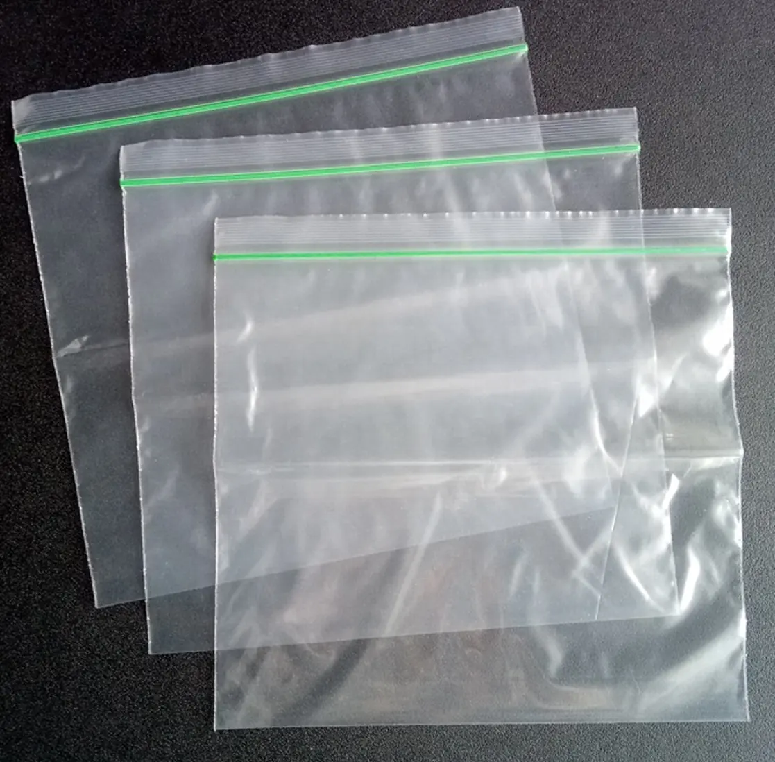 Three clear resealable plastic bags with green zippers on dark surface