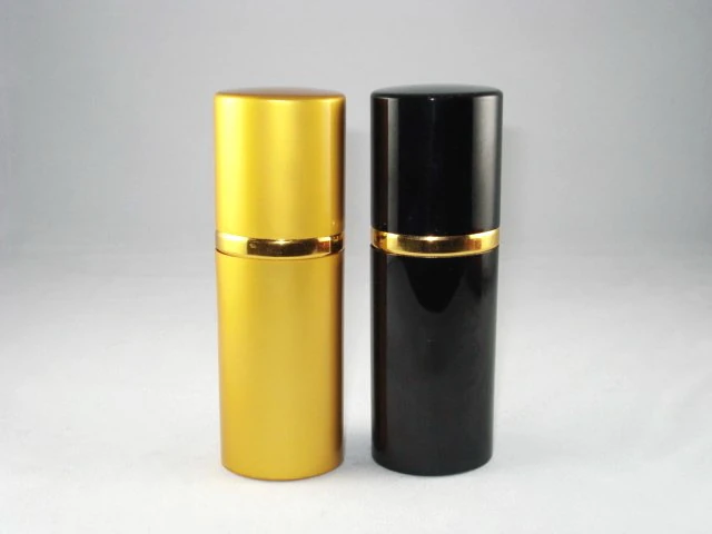 Two cylindrical lipstick cases standing side-by-side, one gold and one black with gold trim, on a clean grey background.