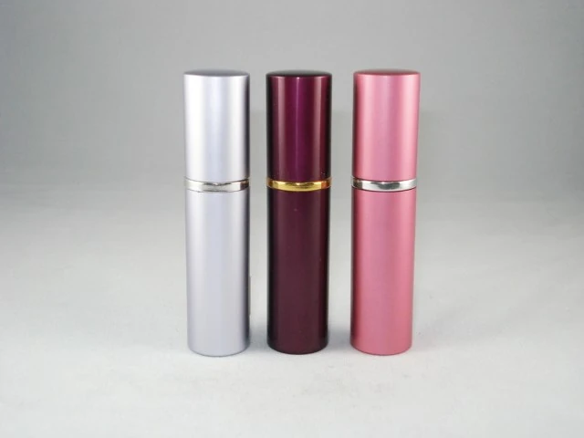 Three cylindrical cosmetic packaging tubes in silver, dark purple, and pink standing upright on a light grey background.