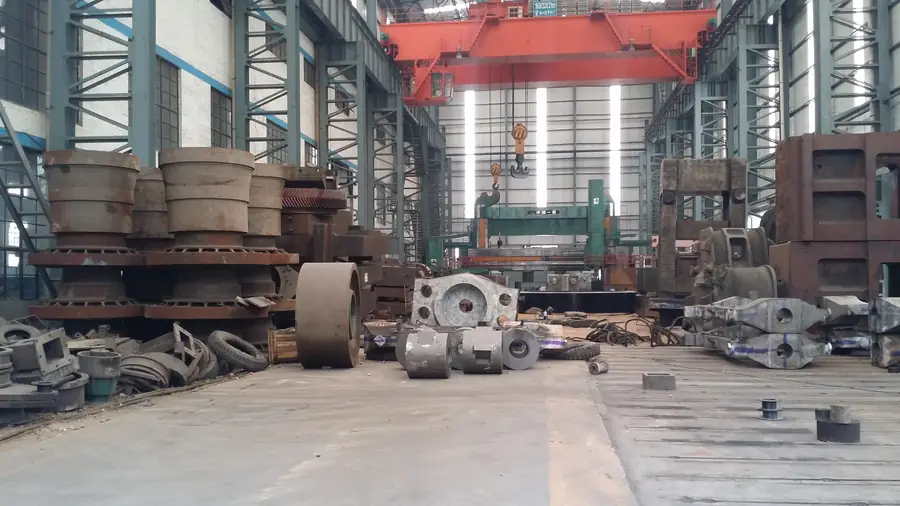 Heavy castings and machined components on a workshop floor under an overhead crane