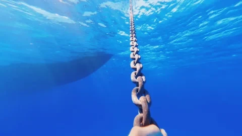 An underwater view looking up a mooring chain towards the surface with a ship's hull visible on the left