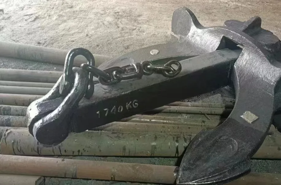 A heavy black metal anchor with a chain attached, resting on top of several pipes