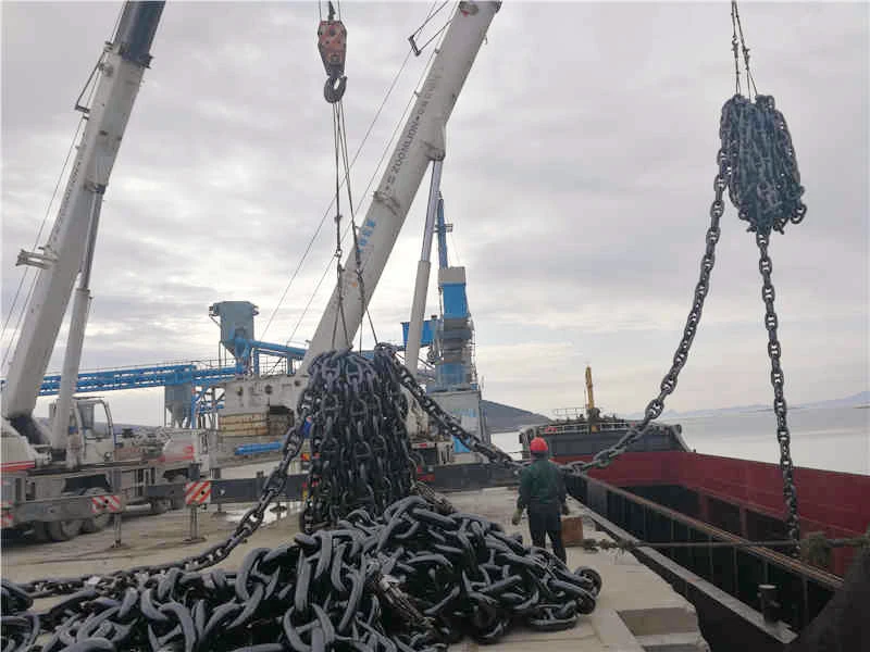 Large piles of heavy industrial anchor chain links being lifted by a crane onto a barge