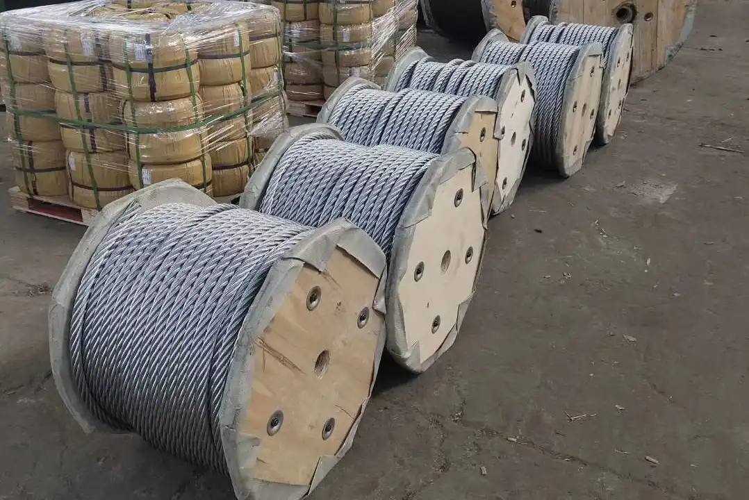 Wooden reels wound with steel wire rope lined up in a warehouse, with wrapped coils stacked on pallets behind