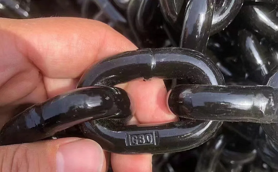 Close-up of a hand holding black alloy steel lifting chain links, one link stamped G80