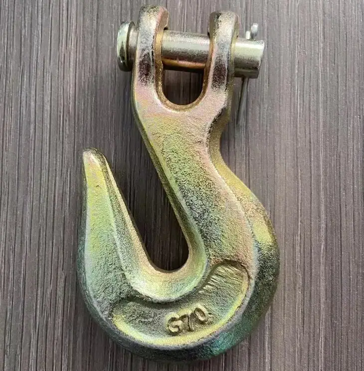 Gold-plated G70 clevis lifting hook with safety latch on a wooden surface