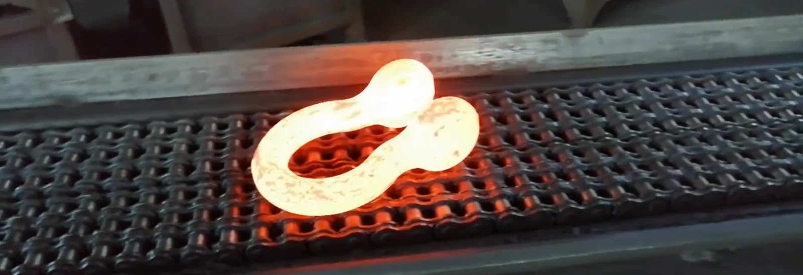 Glowing hot forged metal link on a roller conveyor inside a forge workshop