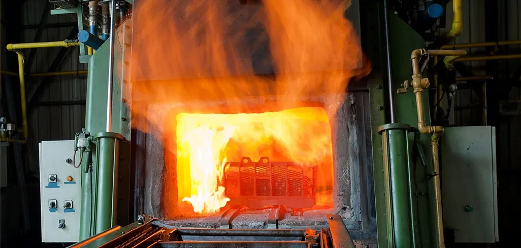 Large industrial furnace glowing with bright orange flames and heat inside a factory