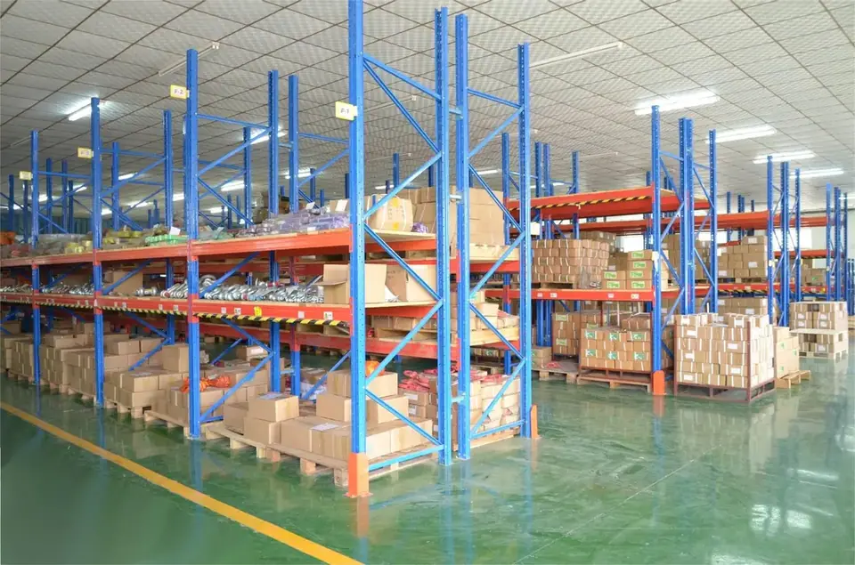 Warehouse interior with blue and orange pallet racks filled with cardboard boxes and goods on a green floor