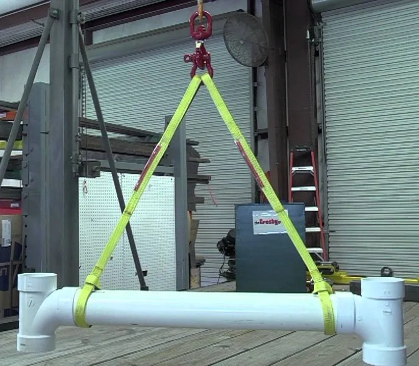 Yellow lifting slings suspending a white pipe assembly from a red hook in a workshop