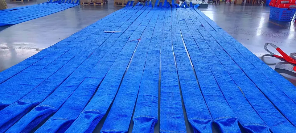 Rows of blue flat webbing lifting slings laid out on a factory floor