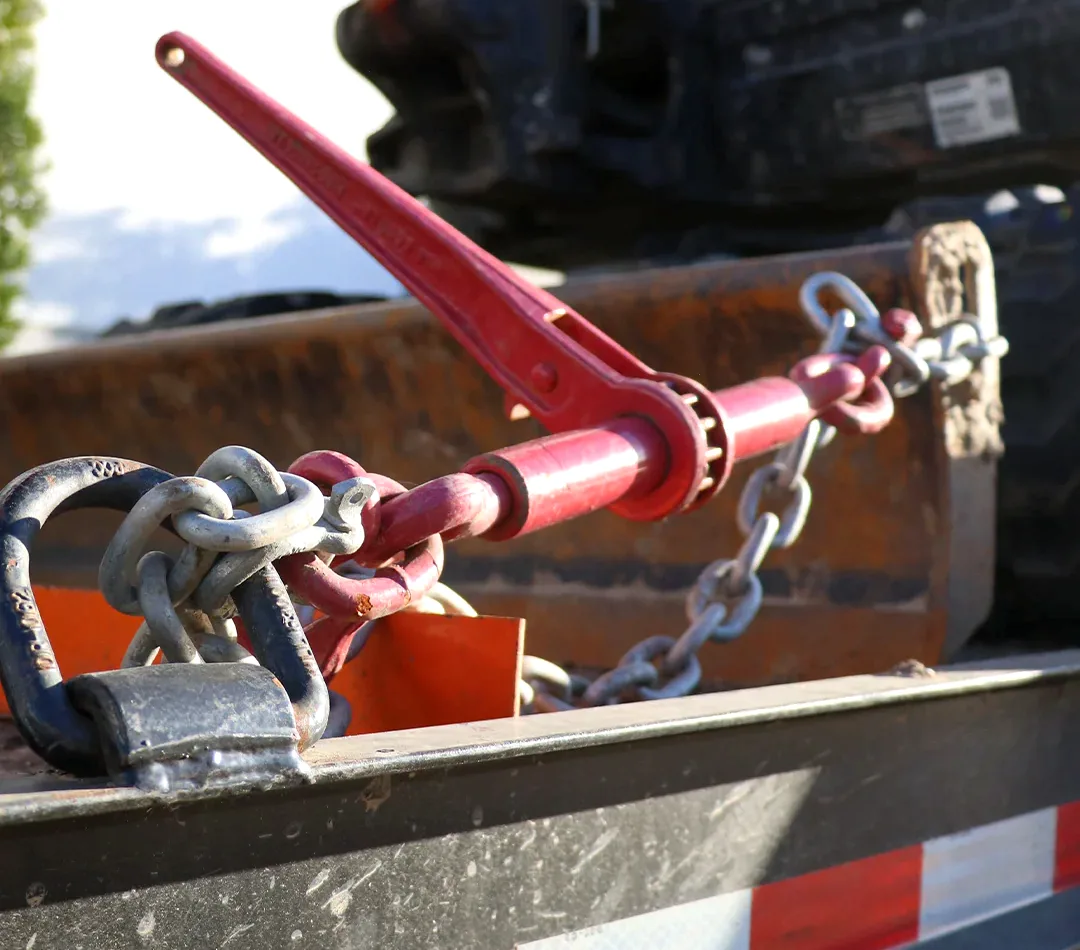 A red industrial lever binding mechanism attached to metal chains and hooks on a truck bed