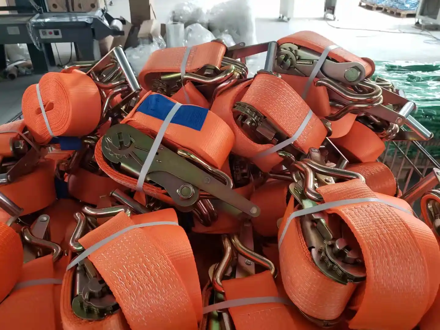 Stack of orange ratchet tie-down straps with metal buckles and hooks bundled in a warehouse