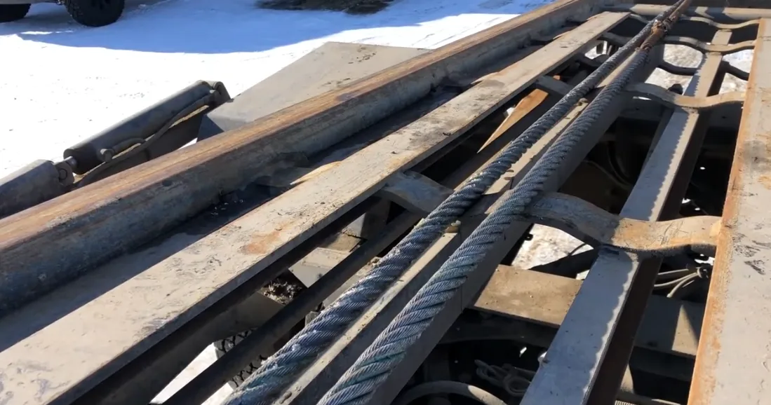 Close-up of a thick steel wire rope lying across a rusty metal machine frame outdoors in snow