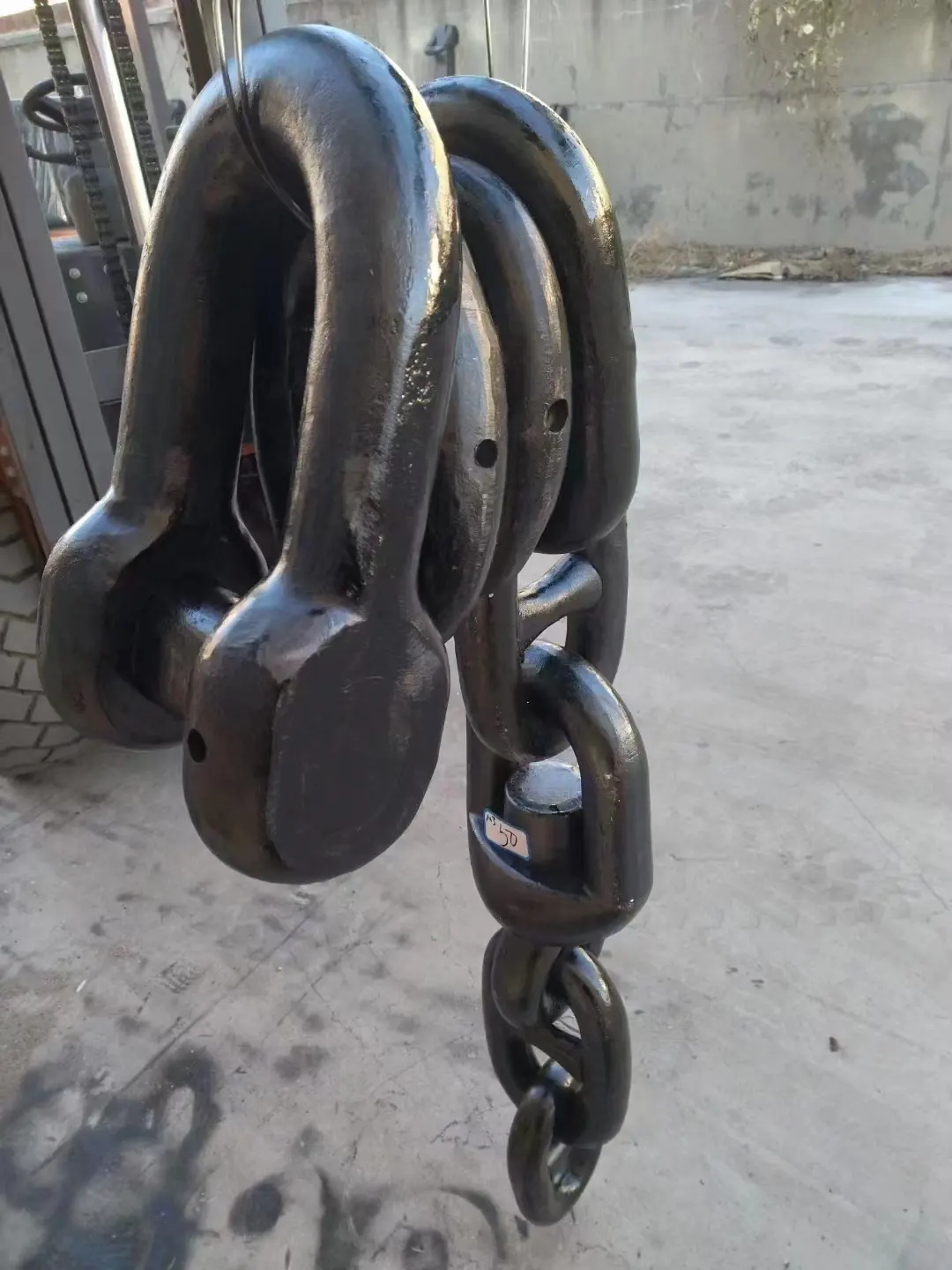 Large black painted anchor shackles and heavy chain links hanging in an industrial yard
