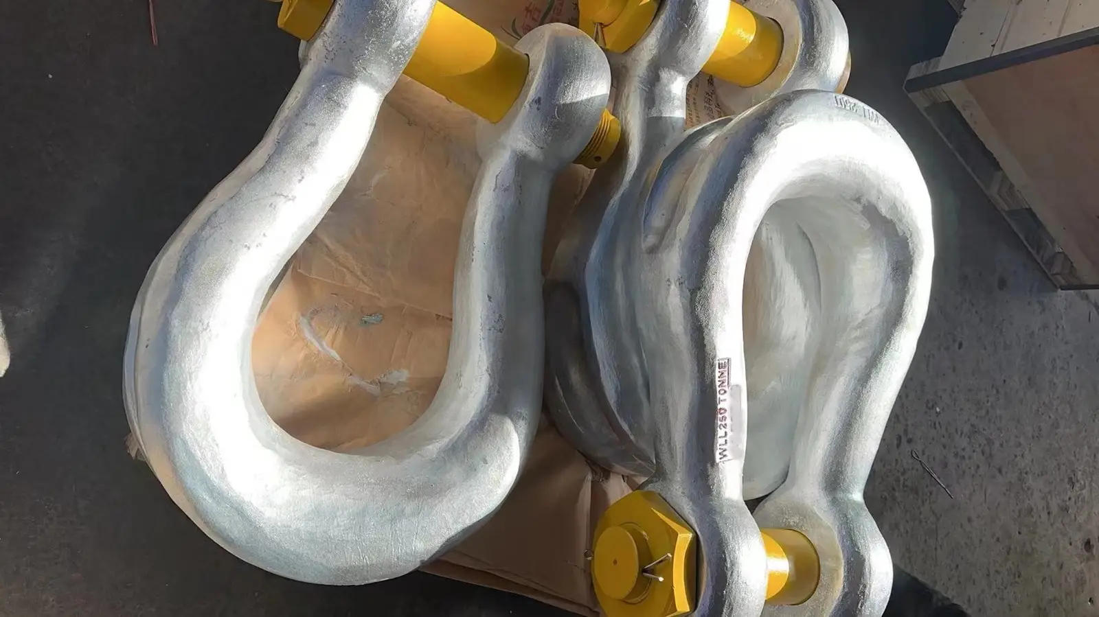 Close-up of two large galvanized steel shackles with yellow pins resting on a wooden crate