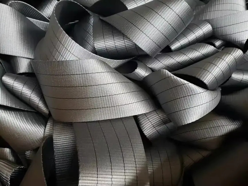 Close-up pile of coiled gray woven webbing straps with thin black grid threads woven through them