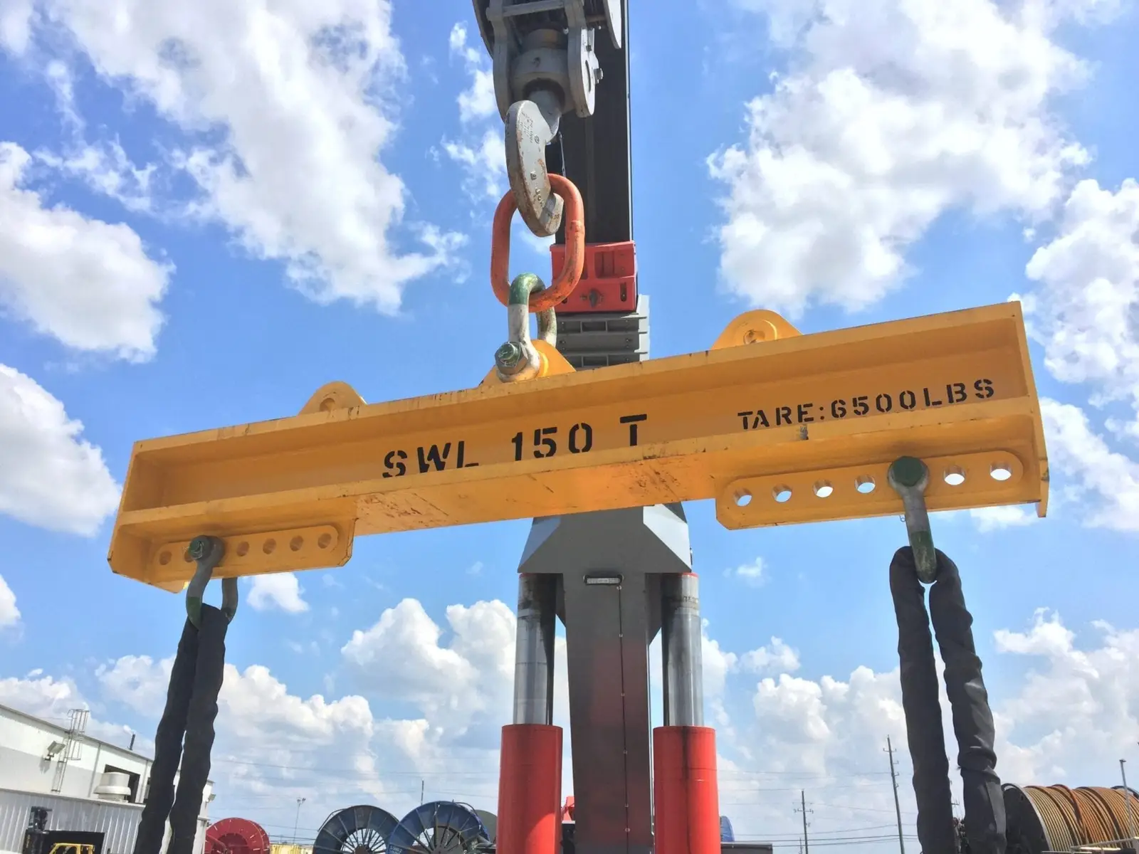 Yellow lifting spreader bar with 150T SWL rating suspended by hook against a blue sky