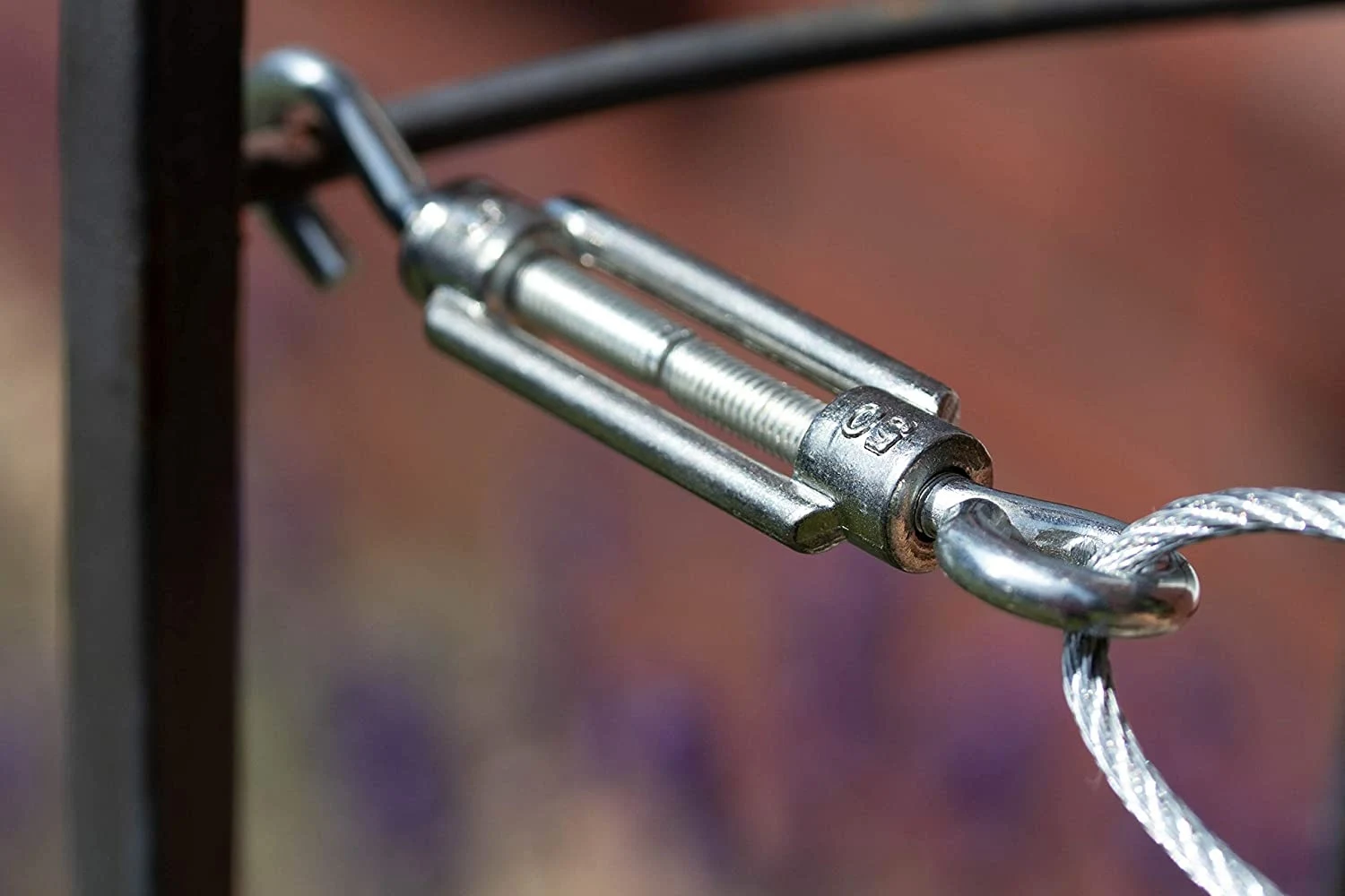 Close-up of a metal turnbuckle connecting a wire rope to a post