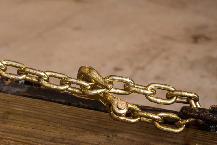 Brass chain hook and links attached to a rusty metal bar on wood