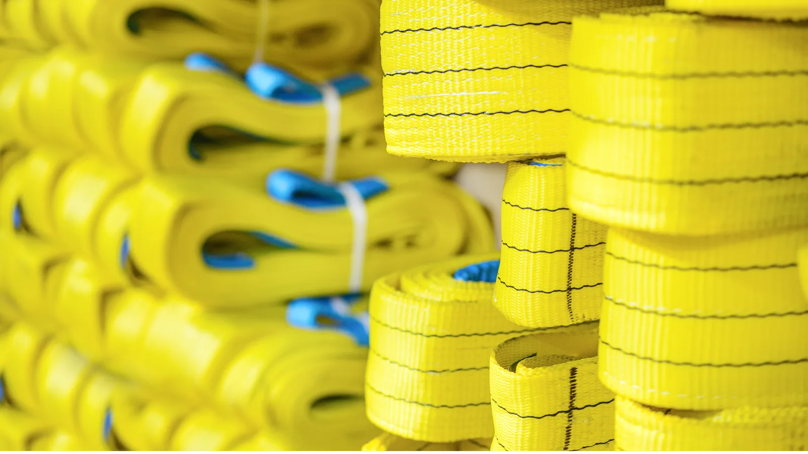 Bundles of yellow webbing lifting slings with blue edge protectors stacked closely together