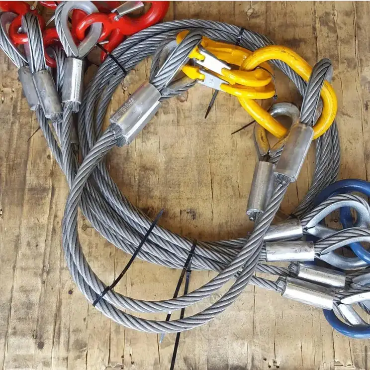 Coiled wire rope slings with red, yellow, and blue metal fittings resting on a wooden surface