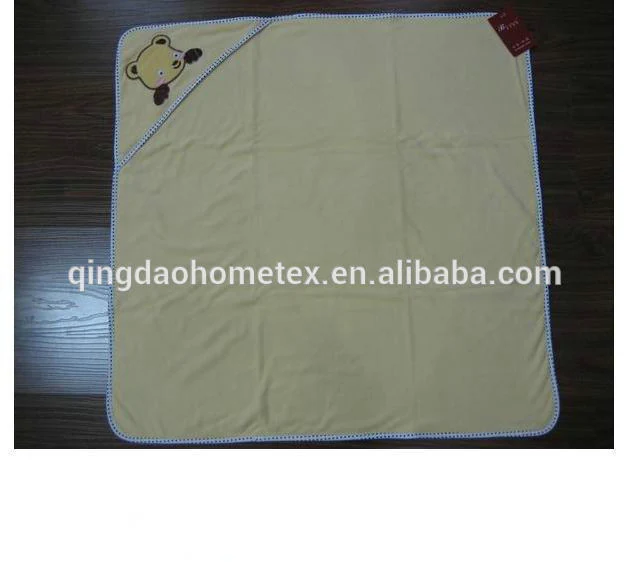 A folded cream-colored baby blanket with a blue stitched edge and an embroidered bear face on the corner.