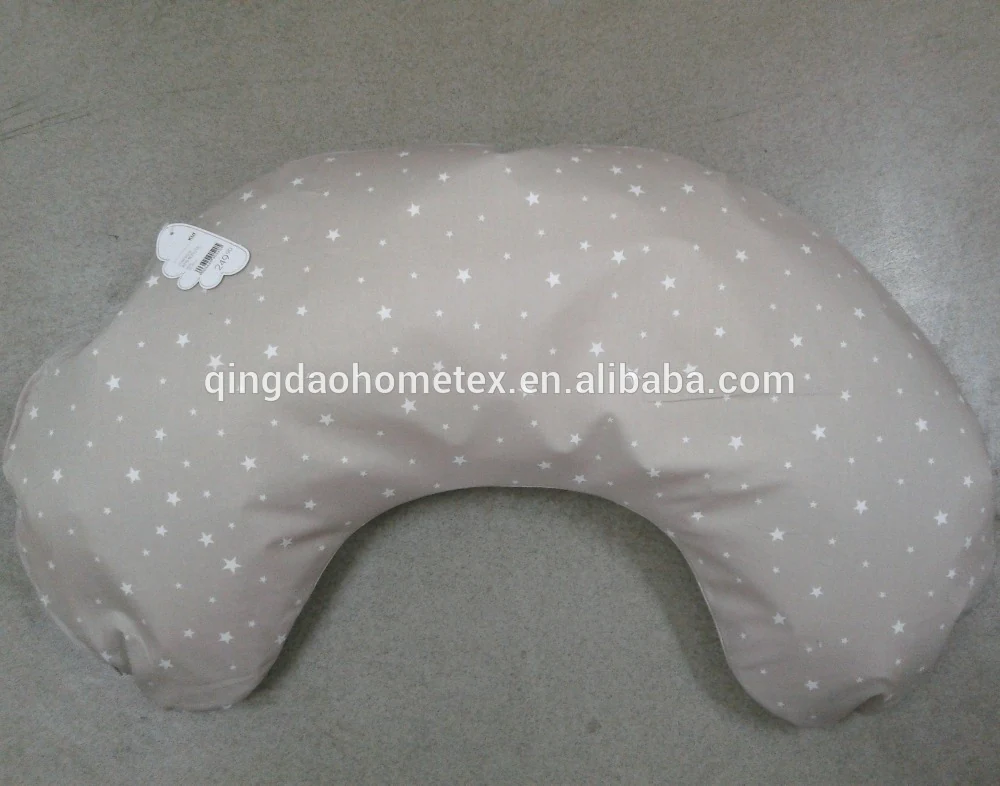 Beige crescent-shaped nursing pillow with white star print and fabric tag, photographed lying on a floor