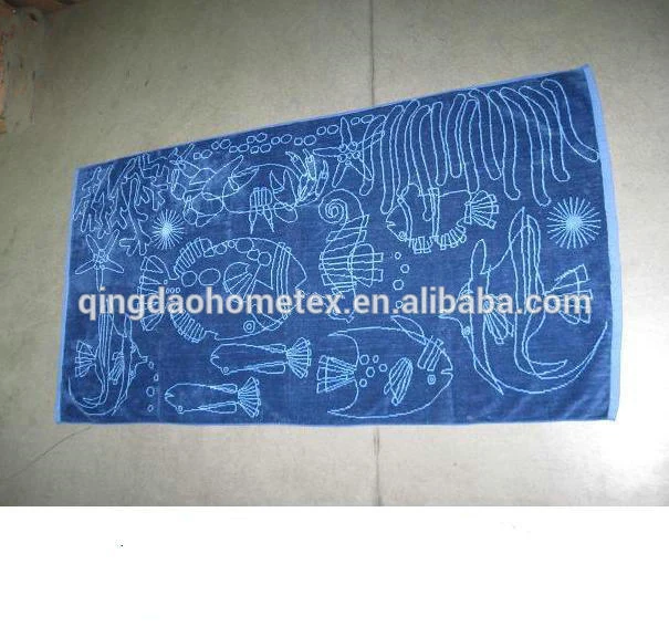 Blue beach towel printed with white sea-creature outlines: fish, seahorse, starfish and jellyfish, photographed on a concrete floor