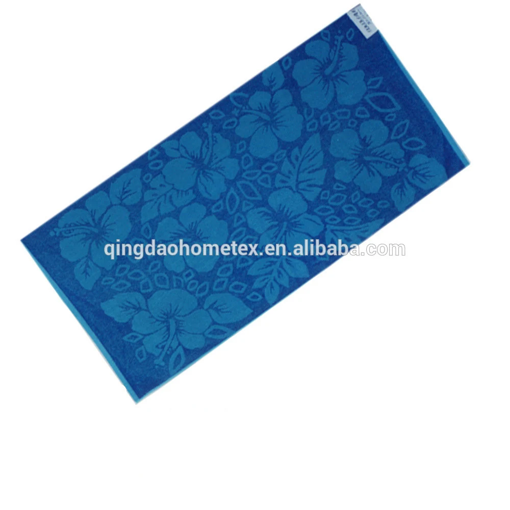 Blue jacquard beach towel with hibiscus flower pattern and small fabric tag, laid diagonally on white background