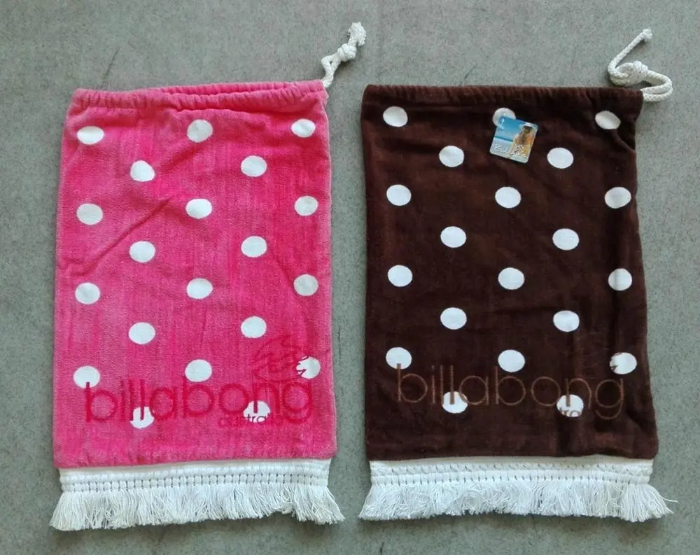 Two polka dot drawstring bags with fringe, one pink and one brown, lying on a gray concrete floor.
