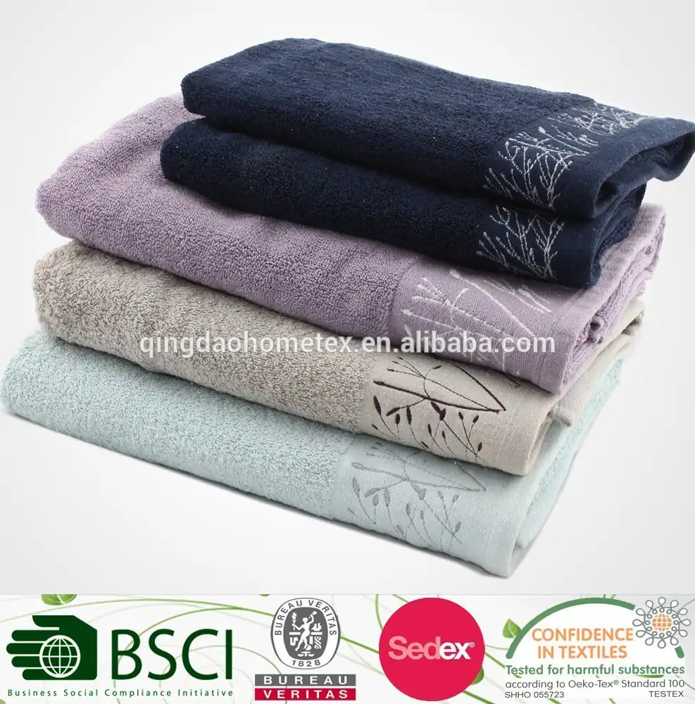 Stack of folded towels in navy, lavender, beige and mint with embroidered leaf borders on a light background