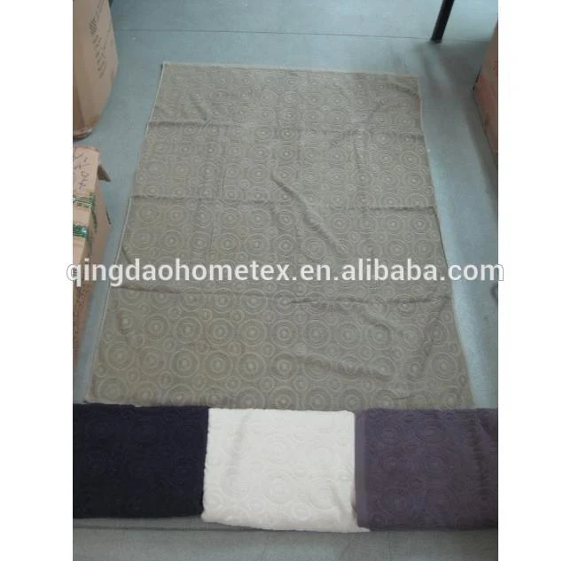Patterned floor mat laid flat on warehouse floor beside cardboard boxes, with folded fabric swatches at the bottom edge