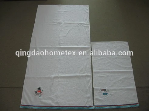 Two white towels with small embroidered motifs and checkered border trim laid flat on a gray surface