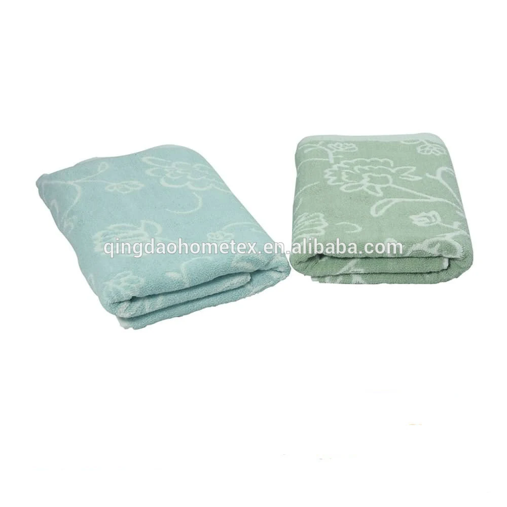 Two folded floral-jacquard towels, one light blue and one sage green, on a white background