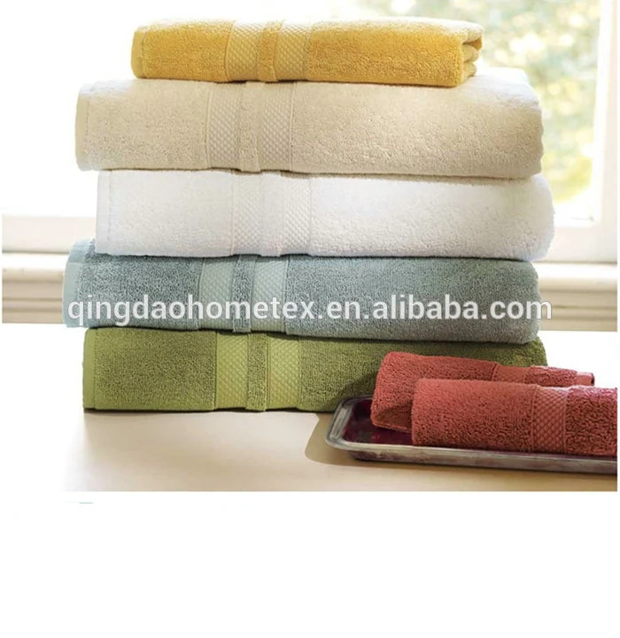 Stack of folded towels in yellow, cream, white and green beside rolled pink and maroon towels on a tray