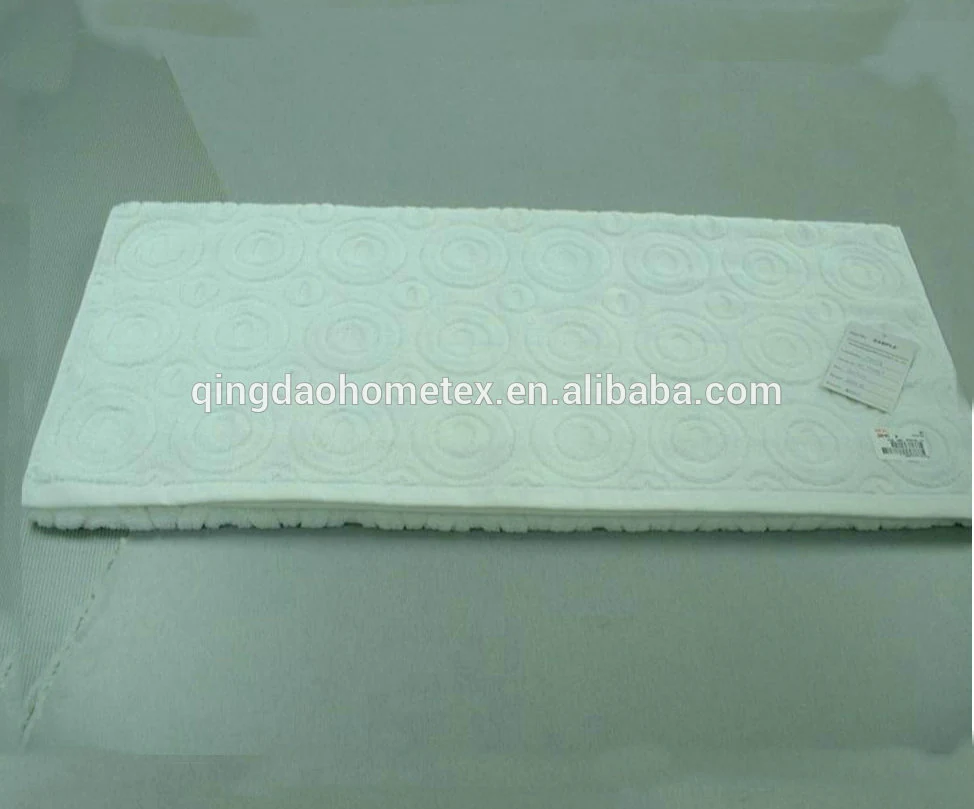 White bath mat with embossed circular pattern photographed at an angle on a plain grey surface