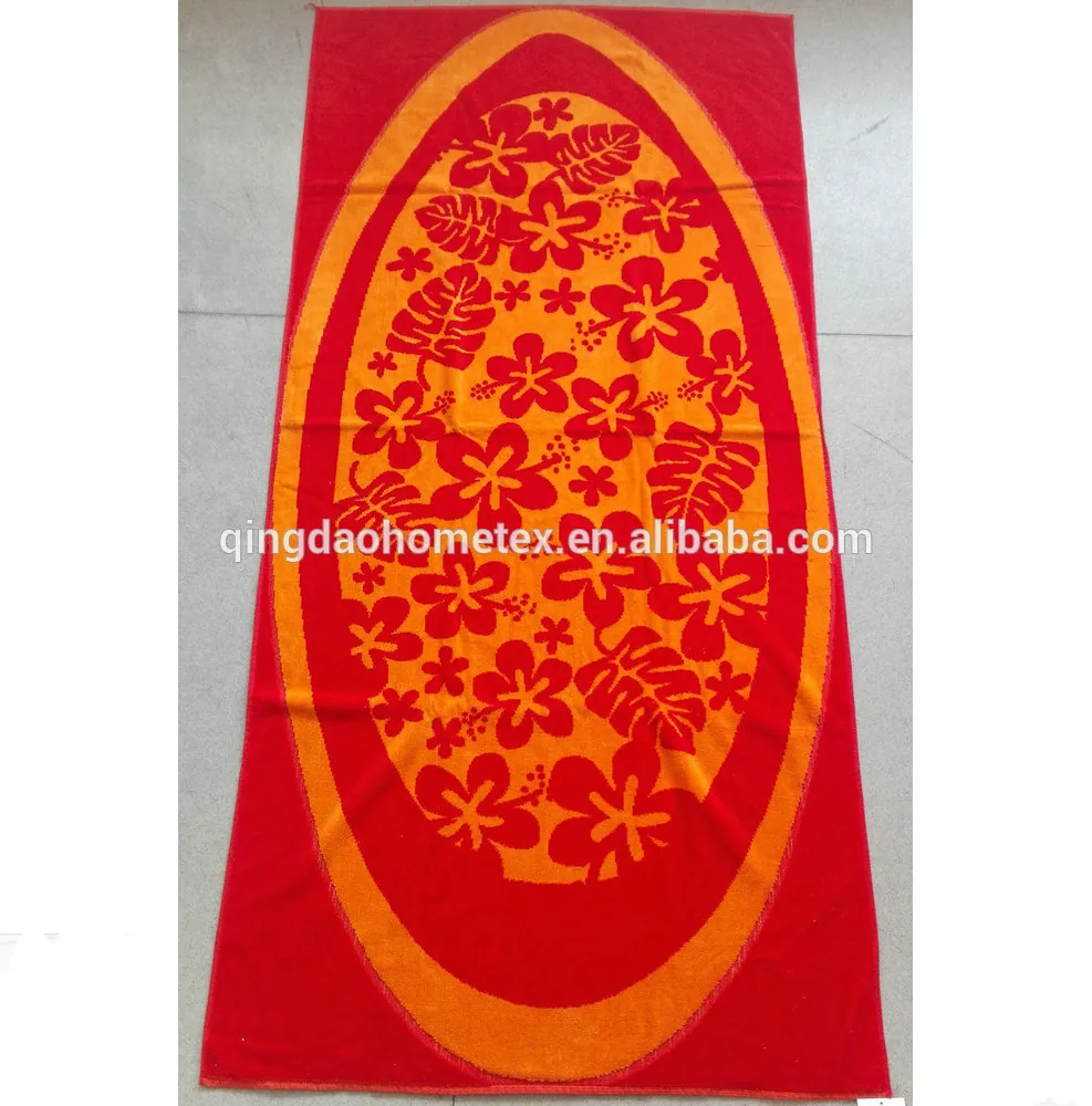 Red beach towel with orange oval panel printed with red hibiscus flowers and leaves, lying on a beige tiled floor