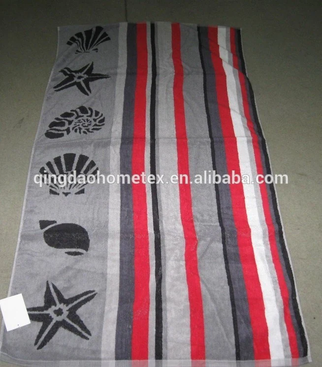 Grey striped beach towel with black printed starfish and seashell motifs, shown flat on a dark floor