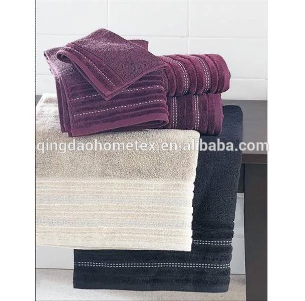 Stacked folded cotton towels in burgundy, cream and dark navy with stitched stripes against a white tiled wall