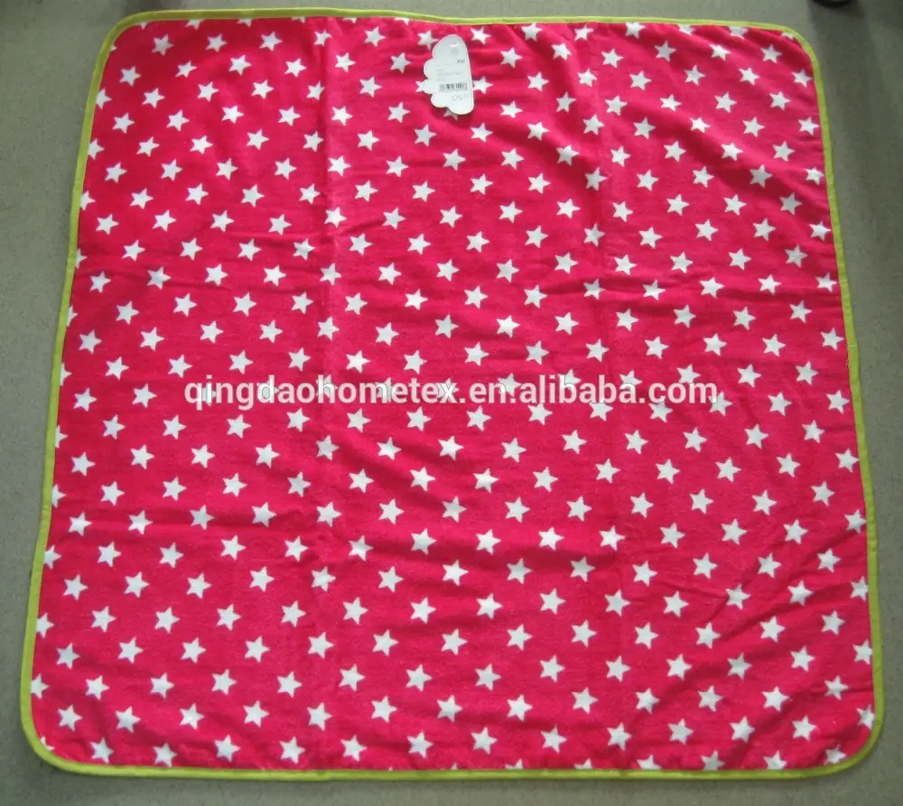 Pink fleece blanket with white star print and green binding laid flat on floor