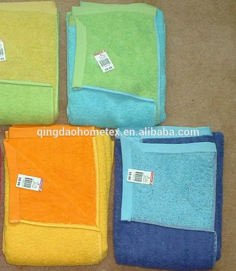 Five folded terrycloth towels in yellow, green, blue, and orange colors laid on a carpet floor