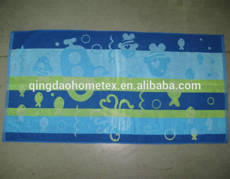 Blue and green striped beach towel printed with fish and sea creatures, laid flat on a concrete floor