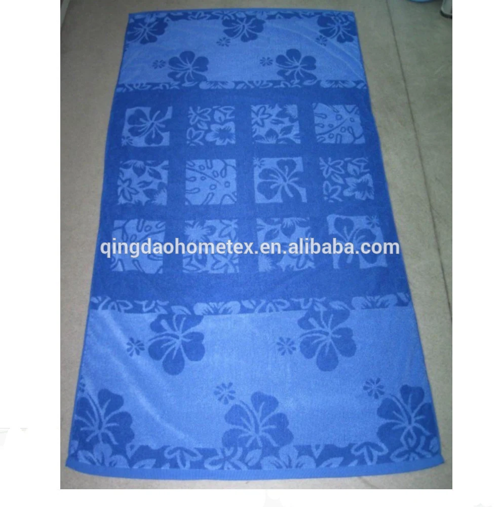 Blue beach towel with floral print in patchwork-style bands, laid flat on a gray floor