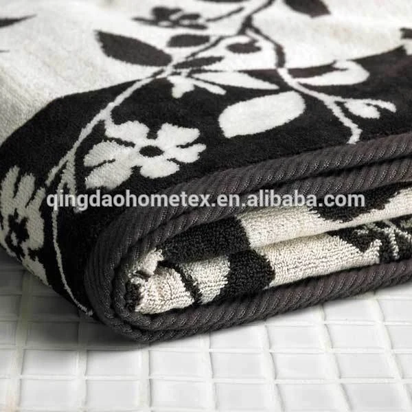 Folded black and white floral jacquard towel with dark trim lying on white tiled surface