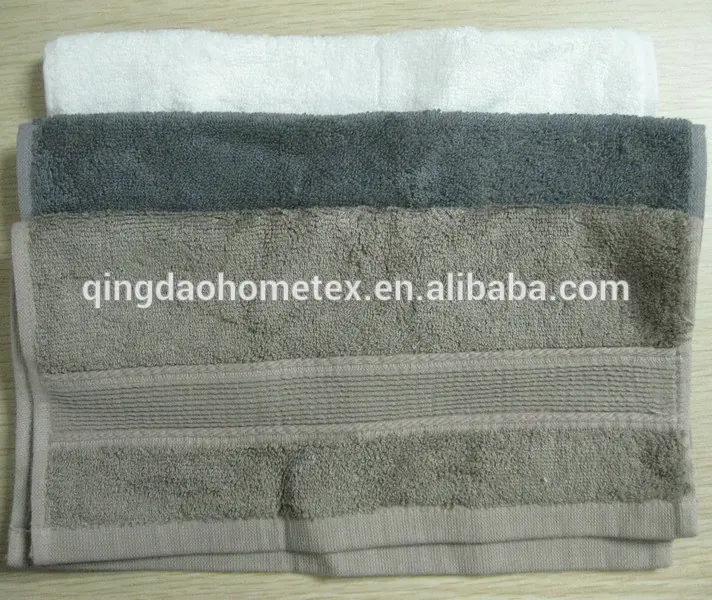 Stack of three folded towels in white, gray, and beige on a wooden surface