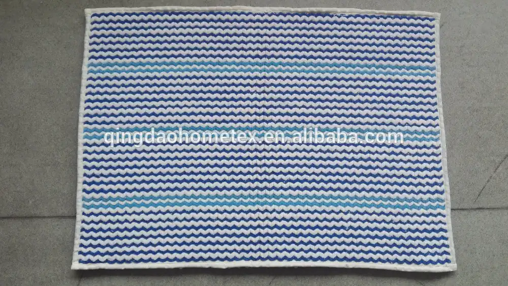 Rectangular woven mat with blue and white zigzag stripes and light blue accent stripes, laid on a gray concrete floor