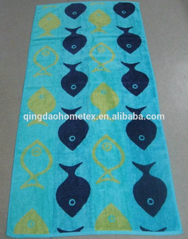 Turquoise beach towel with navy and yellow fish patterns laid flat on a tiled floor