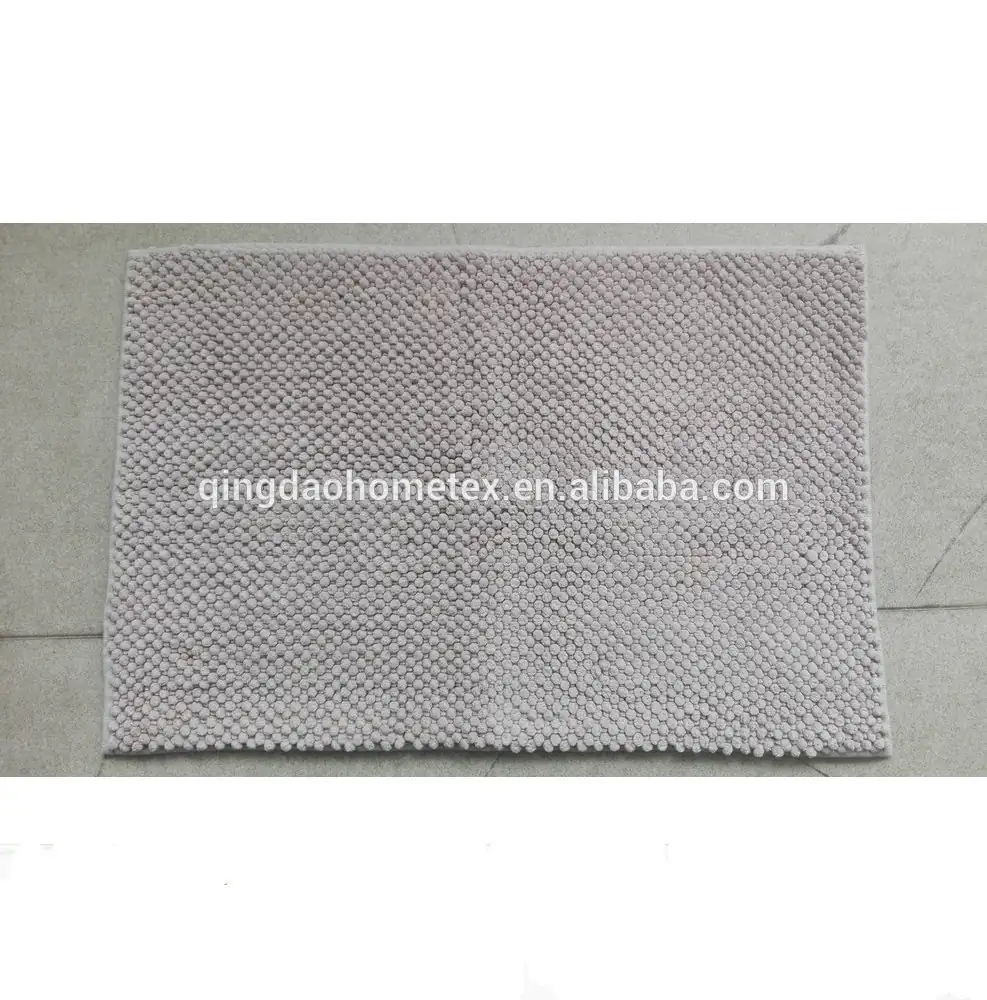 Light gray chenille bath mat with pebbled texture lying on a concrete floor
